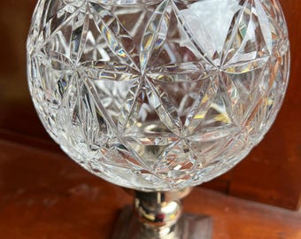May include: A clear glass bowl with a cut crystal design sits on a silver pedestal base. The bowl is round and has a wide opening. The base is square and has a raised center.