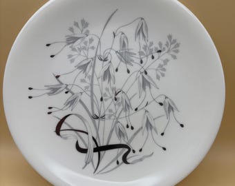 May include: A white ceramic plate with a black and gray floral design. The design features a cluster of stylized flowers and leaves.