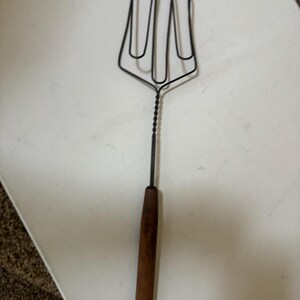 May include: A vintage metal and wood kitchen utensil with a long wooden handle and a four-pronged fork.
