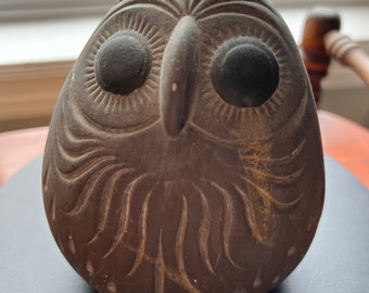 Könnte beinhalten: Eine braune Keramik-Eulenfigur mit detaillierten Schnitzereien und schwarzen Augen. Die Eule sitzt auf einer dunklen Oberfläche.