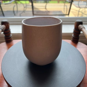 May include: A light gray ceramic mug with a rounded shape sits on a black circular coaster.