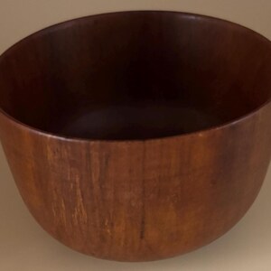 May include: A handcrafted wooden bowl with a rich, dark brown finish. The bowl has a smooth, curved design and a wide opening. The interior is a deep, contrasting shade of brown. This decorative bowl is suitable for serving or display.