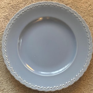 May include: A light blue ceramic plate with a decorative rope-like border. The plate has a smooth, glossy surface and a slightly raised rim. This plate is suitable for serving meals.