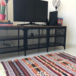 May include: A black metal TV stand with a wood top and a geometric patterned rug in shades of brown, orange, and white.