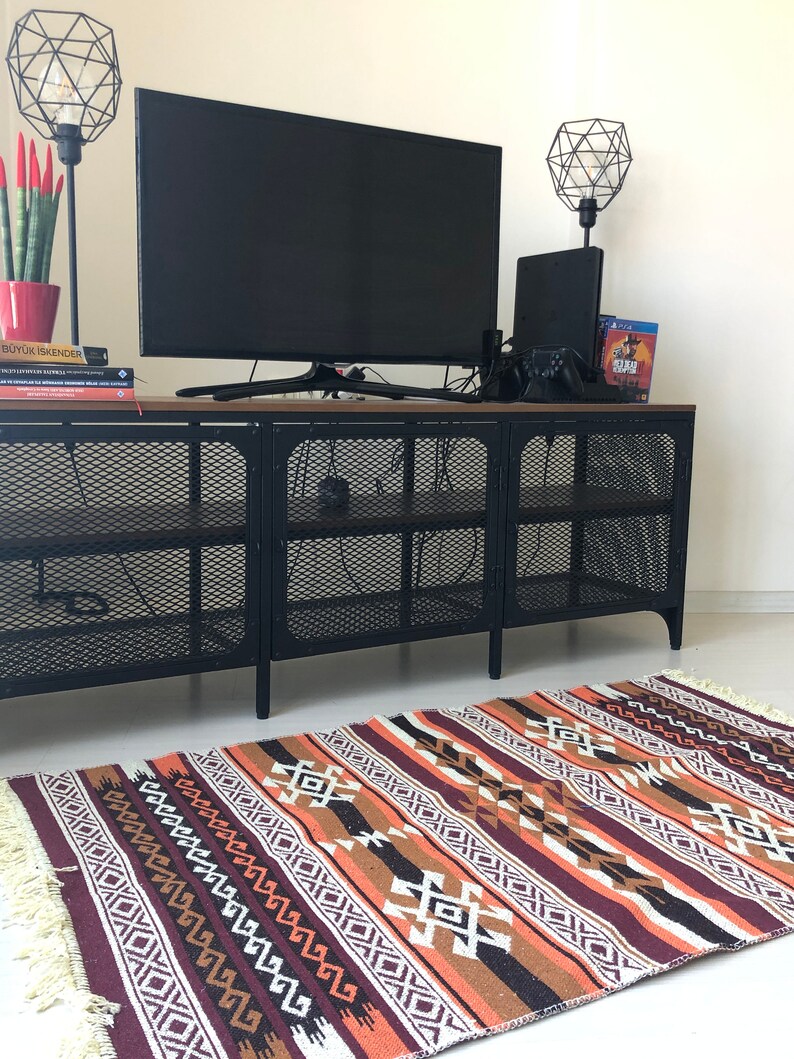 May include: A black metal TV stand with a wood top and a geometric patterned rug in shades of brown, orange, and white.
