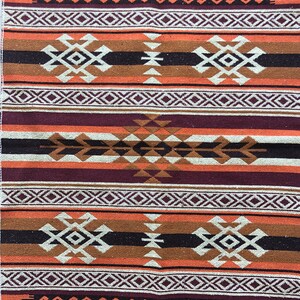 May include: A woven rug featuring a geometric pattern in shades of brown, orange, white, and purple. The rug has a traditional design with repeating motifs.