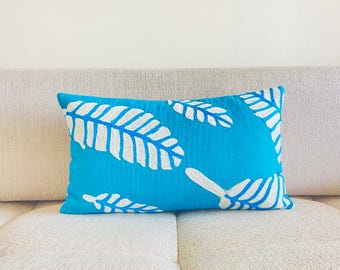 May include: A turquoise blue throw pillow with white embroidered leaf designs.