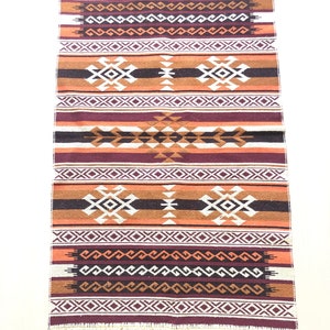 May include: A brown, orange and white woven rug with a geometric pattern. The rug has a fringe on the bottom.