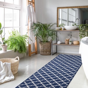 May include: A blue and white patterned bath rug with a geometric design. The rug is placed in a bathroom with a white bathtub, a wooden vanity, and plants.