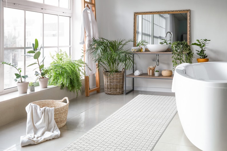May include: A white bathroom with a white bathtub, a white towel, a wooden ladder with a white robe hanging on it, a white rug, and plants in pots.