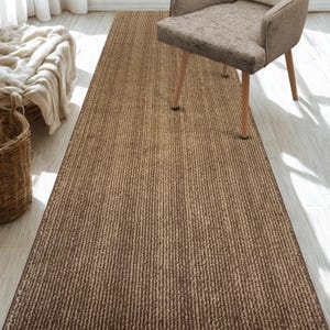 May include: A brown and beige striped runner rug with a textured surface. The rug is placed on a light wood floor and a chair is partially visible in the foreground.