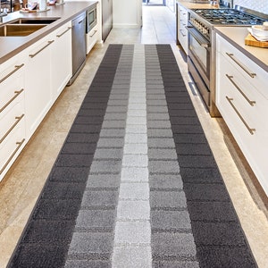 May include: A gray and white striped runner rug with a modern geometric design. The rug is placed in a kitchen between two white cabinets.