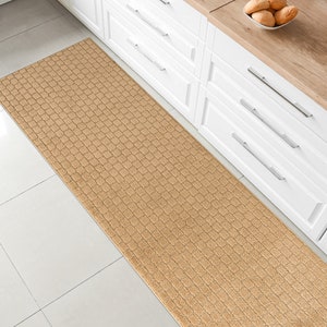 May include: A beige kitchen runner rug with a textured woven pattern. The rug is placed in front of white kitchen cabinets with silver handles.