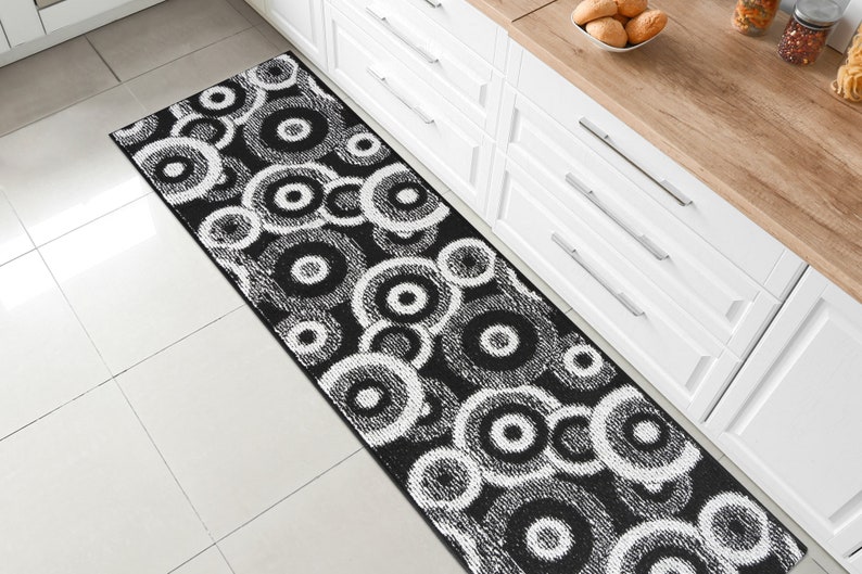 May include: Black and white patterned kitchen runner rug with a circular design. The rug is made of a soft, plush material and is perfect for adding a touch of style to any kitchen.