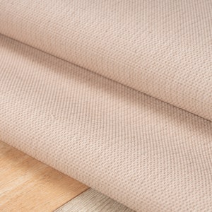 May include: Close-up of a beige woven rug with a textured surface. The rug is folded in half, showing the underside of the fabric.