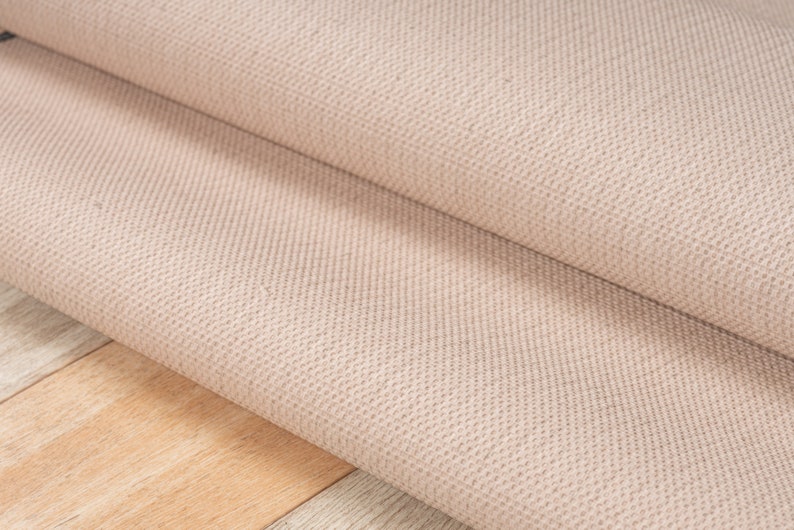 May include: Close-up of a beige woven rug with a textured surface. The rug is folded in half, showing the underside of the fabric.