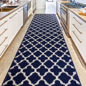 May include: A long, rectangular navy blue and white patterned rug in a kitchen setting. The rug features a repeating diamond trellis design. The rug is placed between white cabinets and a stainless steel appliance.