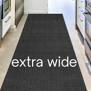 May include: A dark gray, extra wide kitchen runner rug with a repeating geometric pattern. The rug is rectangular and placed in a kitchen with white cabinets and stainless steel appliances. The text "extra wide" is displayed on the rug.