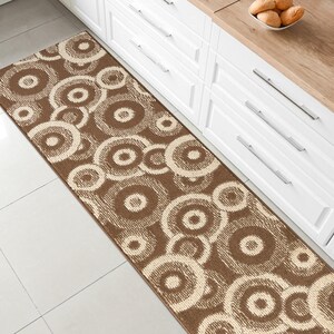 May include: A brown and cream runner rug with a circular pattern. The rug is placed in a kitchen with white cabinets and a wood countertop.