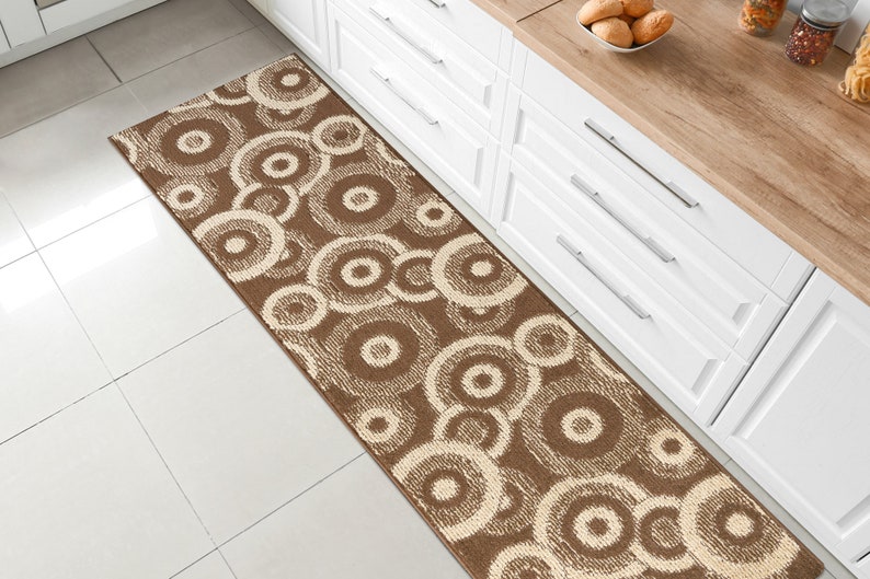 May include: A brown and cream runner rug with a circular pattern. The rug is placed in a kitchen with white cabinets and a wood countertop.