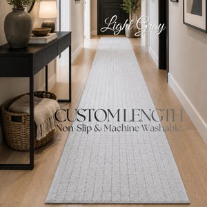 May include: A light gray runner rug with a grid pattern, featuring the text Light Gray, CUSTOM LENGTH, and Non-Slip & Machine Washable. The rug is positioned lengthwise on a wooden floor, extending from the foreground toward a dark door.