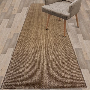 May include: A brown and beige striped runner rug with a subtle textured pattern. The rug is placed on a light wood floor.