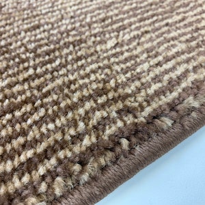 May include: Close-up of a brown and beige striped rug with a woven edge. The rug has a soft, fuzzy texture.