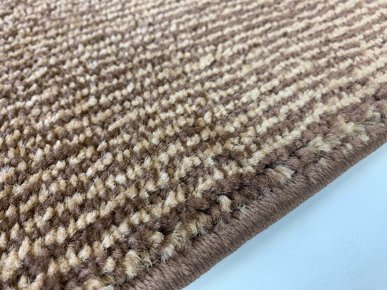 May include: Close-up of a brown and beige striped rug with a woven edge. The rug has a soft, fuzzy texture.