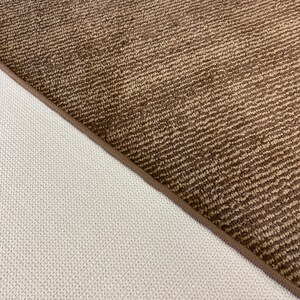 May include: Close-up of the back side of a brown rug with a textured pattern. The rug has a white backing.