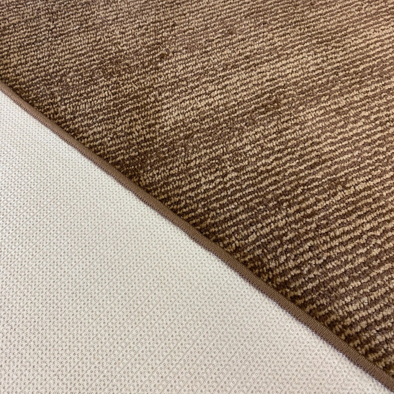 May include: Close-up of the back side of a brown rug with a textured pattern. The rug has a white backing.