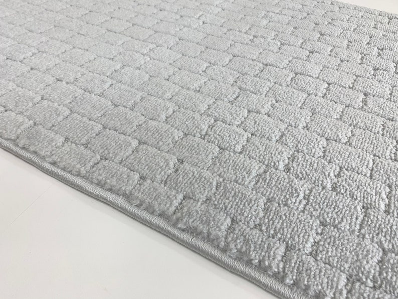 May include: A gray, textured, rectangular bath mat with a subtle pattern. The mat has a stitched edge.