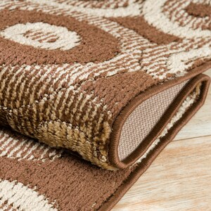 May include: Close-up of a brown and beige area rug with a geometric pattern. The rug has a brown border and is folded in half.