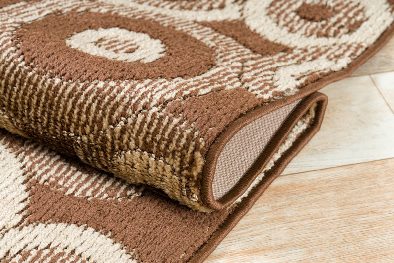 May include: Close-up of a brown and beige area rug with a geometric pattern. The rug has a brown border and is folded in half.