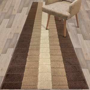 May include: A brown and beige striped runner rug with a white stripe down the center. The rug is on a wood floor and a chair is sitting on the rug.