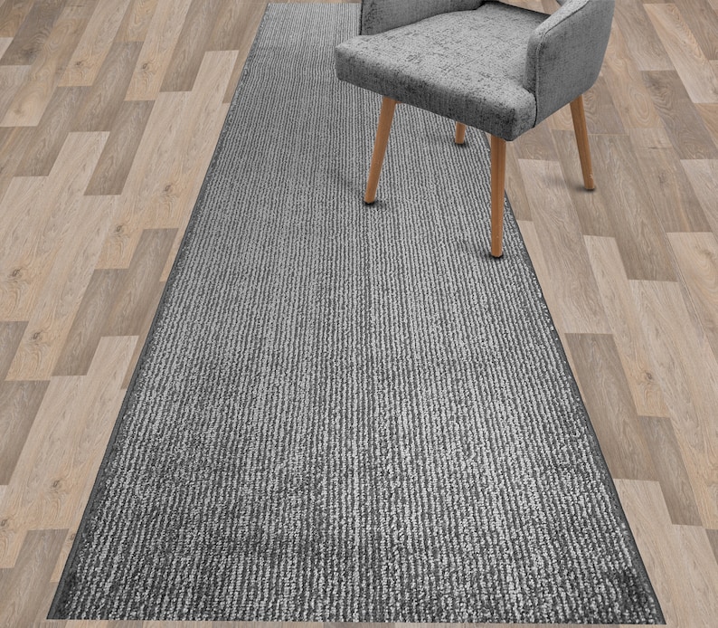 May include: A gray and white striped runner rug with a subtle sheen. The rug is placed on a wood floor and a gray chair is sitting on top of the rug.