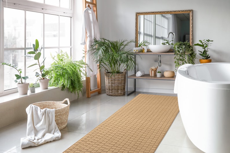 May include: A light brown bath mat with a woven texture, placed in a bathroom with a white bathtub, a wooden shelf with a sink, and plants.