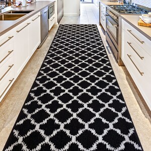 May include: Black and white geometric patterned runner rug in a kitchen setting. The rug is placed between two white kitchen cabinets with gold handles.