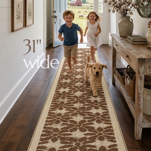 May include: A long rectangular runner rug featuring a repeating brown floral pattern on a cream background. The rug is 31 inches wide and is positioned on a dark wood floor in a hallway. The design consists of stylized flower shapes.