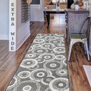 May include: A gray and white patterned runner rug with a circular design. The rug is placed in a hallway with hardwood floors and a wooden chair.
