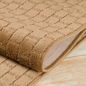 May include: A close-up of a brown, textured rug with a subtle pattern. The rug is folded in half, revealing a beige backing.
