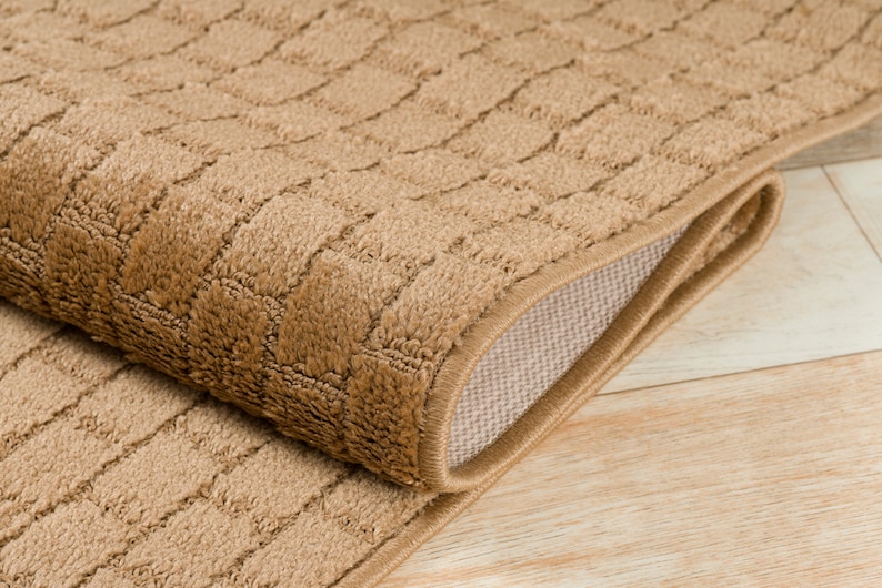 May include: A close-up of a brown, textured rug with a subtle pattern. The rug is folded in half, revealing a beige backing.