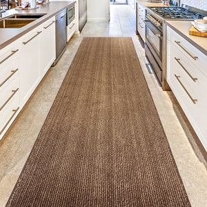 May include: A brown and beige striped kitchen runner rug with a subtle sheen. The rug is placed in a kitchen with white cabinets and a tiled floor.