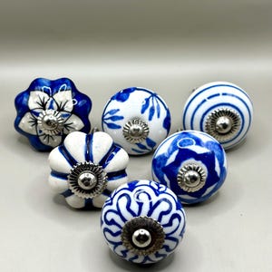 Könnte beinhalten: Sechs Keramik-Schrankknöpfe in Blau und Weiß. Die Knöpfe zeigen florale und geometrische Muster. Jeder Knopf hat eine silberfarbene Metallbasis. Geeignet für Schubladen oder Schränke.