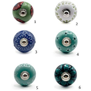 Pode incluir: Uma coleção de seis puxadores de armário de cerâmica em várias cores e padrões. Os puxadores apresentam desenhos florais e são montados com ferragens prateadas. As cores incluem verde, branco, azul e verde-azulado.
