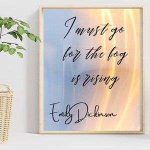 May include: A framed print with a quote by Emily Dickinson: "I must go for the fog is rising". The background is a blurry image of a sunset with orange and yellow hues.