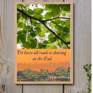 Op de afbeelding: Een ingelijst afdruk met een citaat van Emily Dickinson: "Yet have all roads a clearing at the End". De bovenste helft van de afdruk toont een foto van groene bladeren tegen een heldere lucht. De onderste helft van de afdruk toont een stadsbeeld met een zonsondergang op de achtergrond.