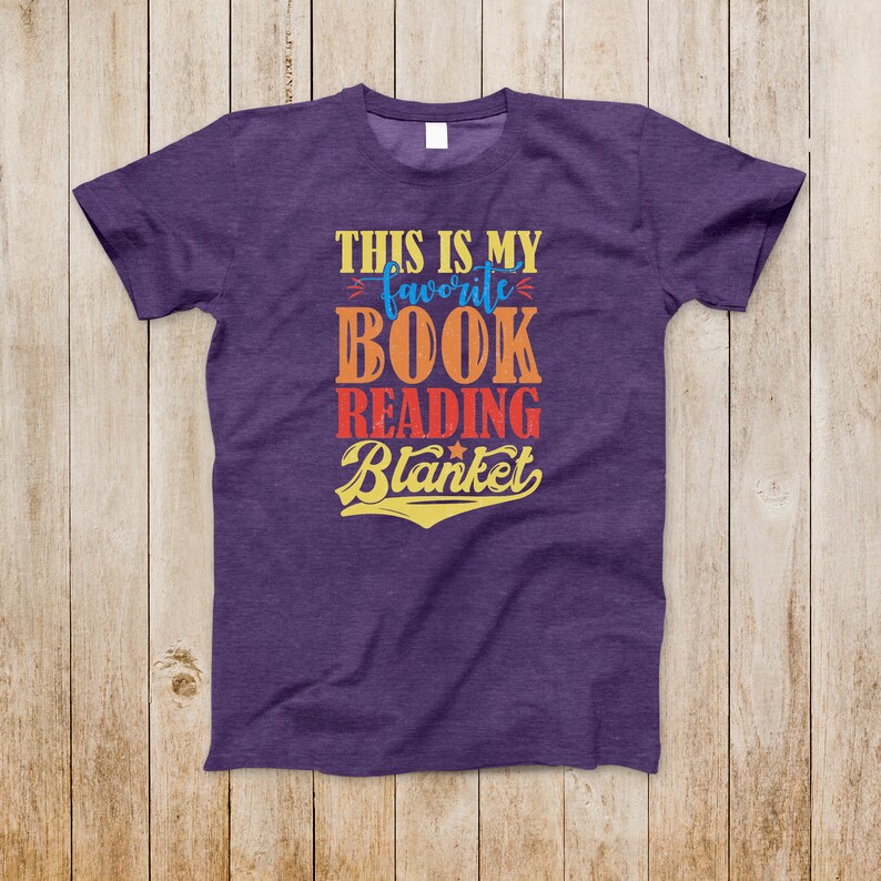 May include: Purple t-shirt with the text "This is my favorite book reading blanket" in a vintage style font with a star.