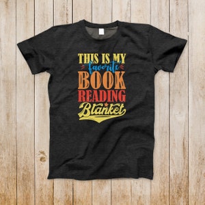 May include: A dark gray t-shirt with the text "This is my favorite book reading blanket" in a retro font with colorful accents.