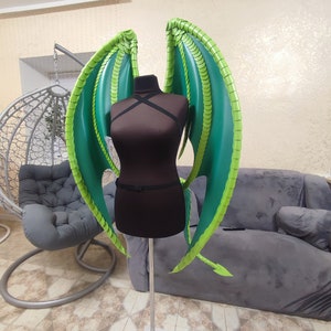 K&ouml;nnte beinhalten: Gr&uuml;ne und lindgr&uuml;ne Drachenfl&uuml;gel aus Schaumstoff, befestigt an einer schwarzen Schaufensterpuppe.