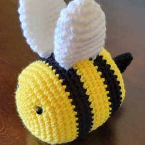 Może przedstawiać: Pluszowa zabawka w kształcie pszczoły, wykonana na szydełku, z żółto-czarnymi paskami, białymi skrzydłami i czarnymi oczami.